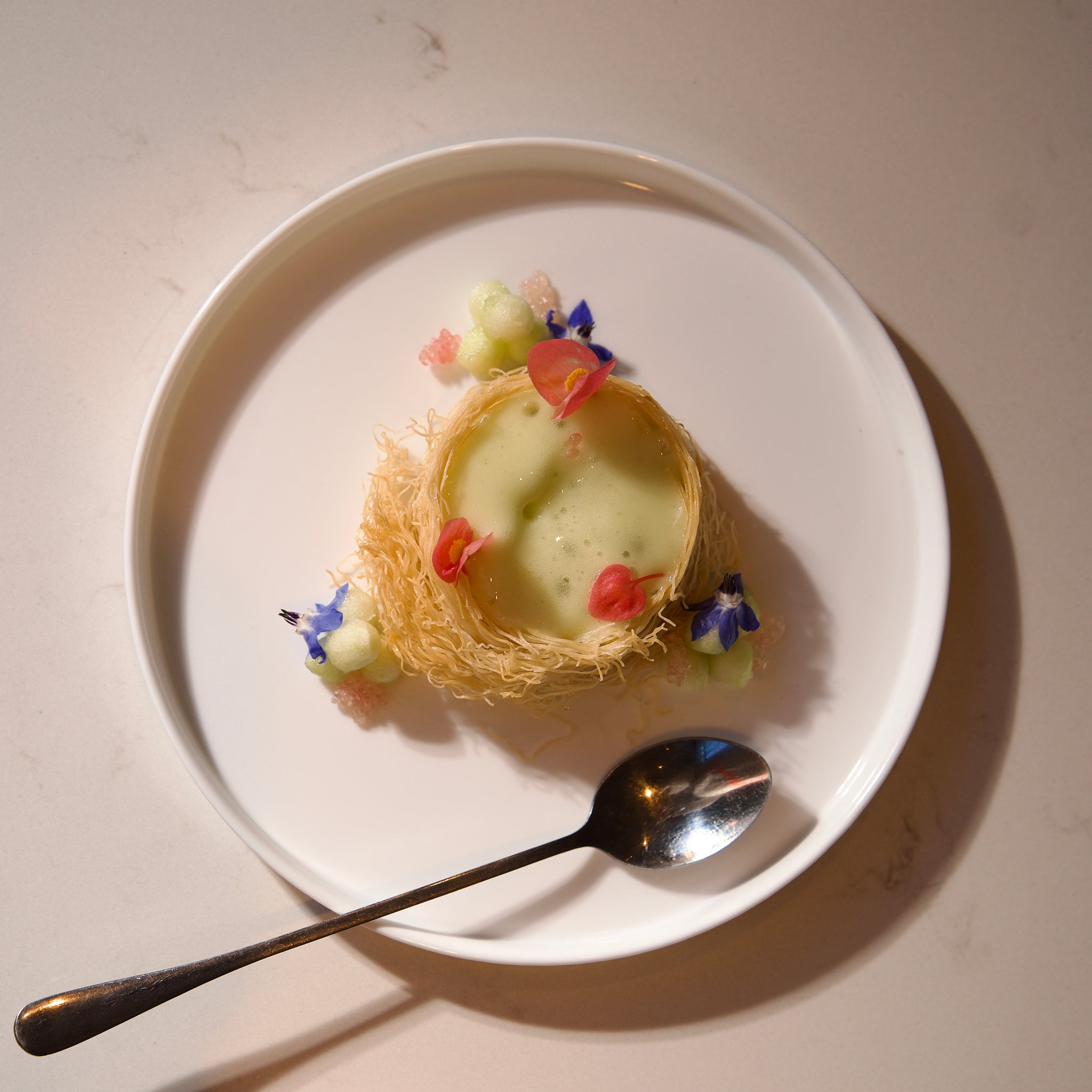 Small dessert in a nest with flowers on a white dessert plate with a spoon