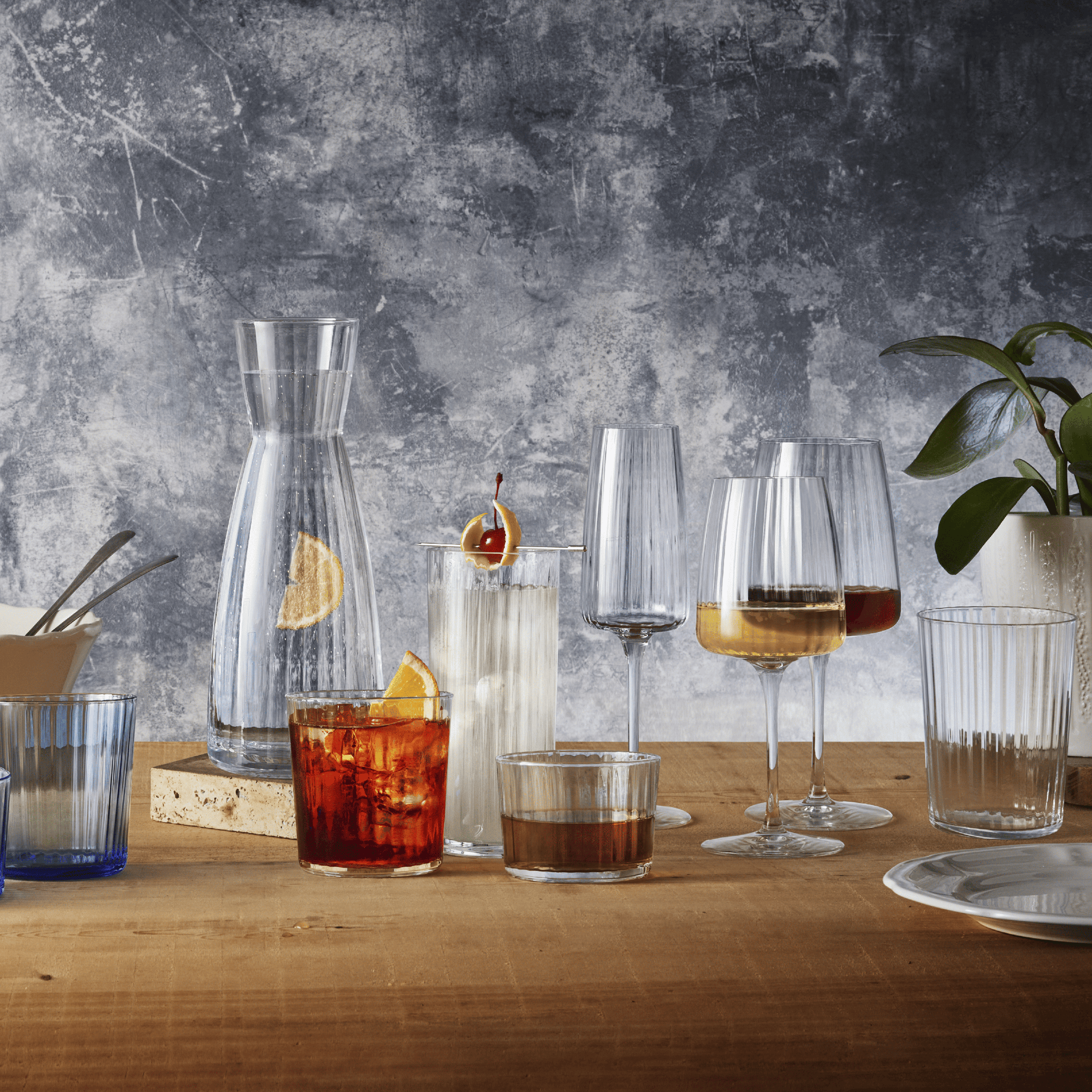 Exclusiva collection glasses and carafe on a wooden table against a textured wall.