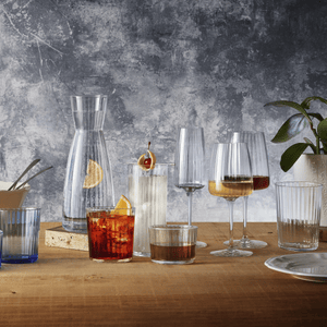 Exclusiva collection glasses and carafe on a wooden table against a textured wall.