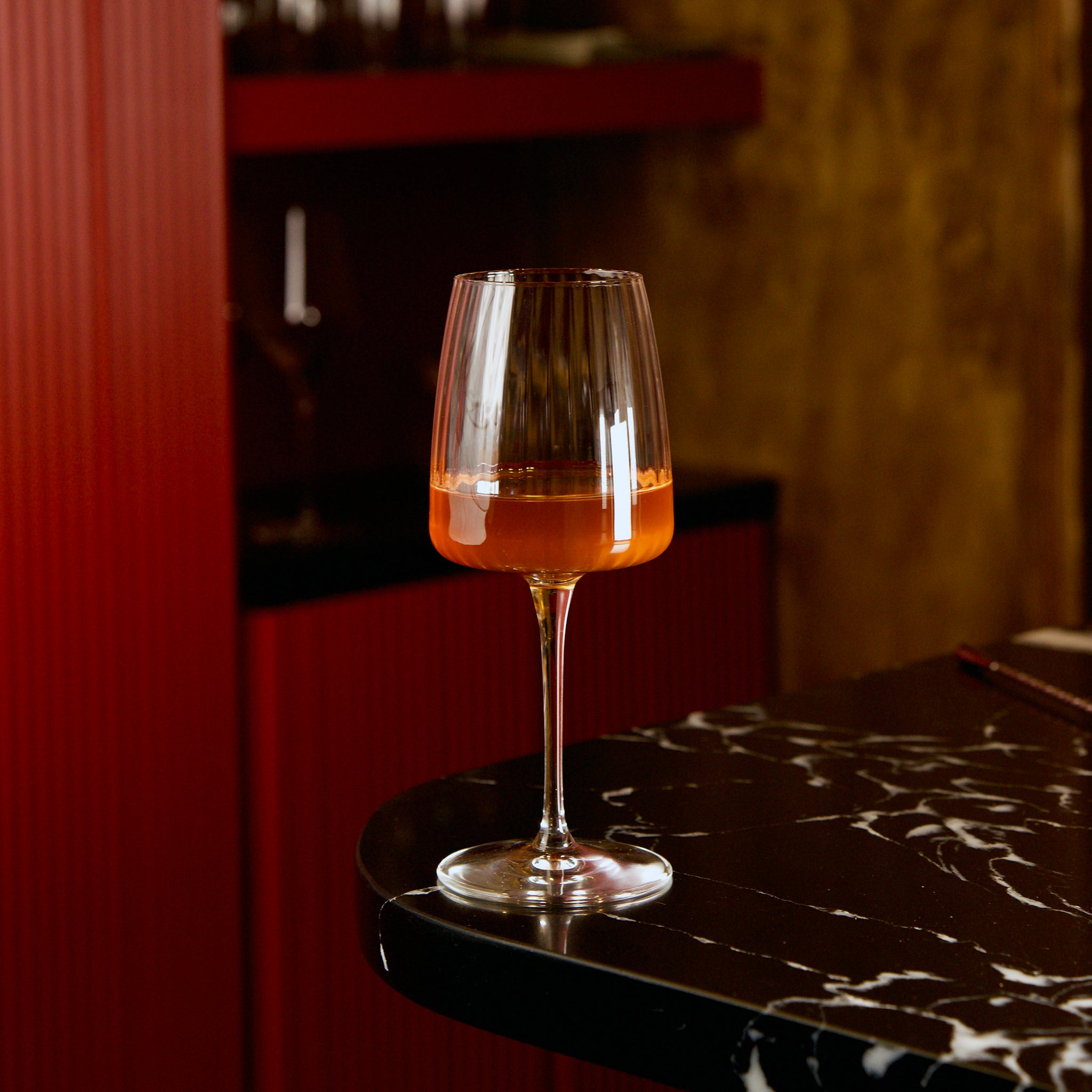 Exclusiva Chardonnay glass with orange wine on a dark marble surface with blurred background