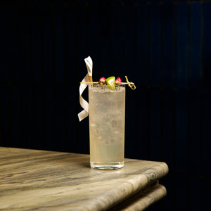 Cocktail in Exclusive Tom Collins glass with colorful garnish on a marble surface against a dark background