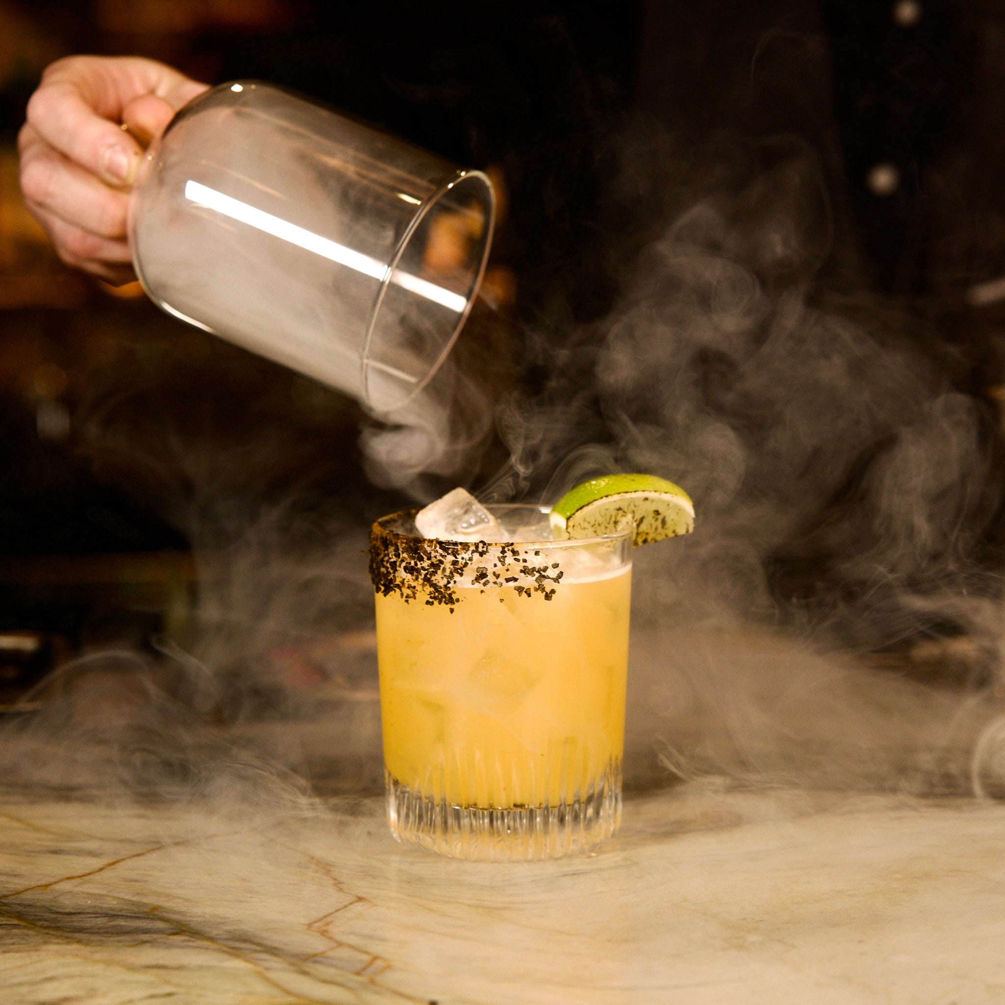 Cocktail being poured in a Graphics DOF glass with a lime wedge and smoke effect