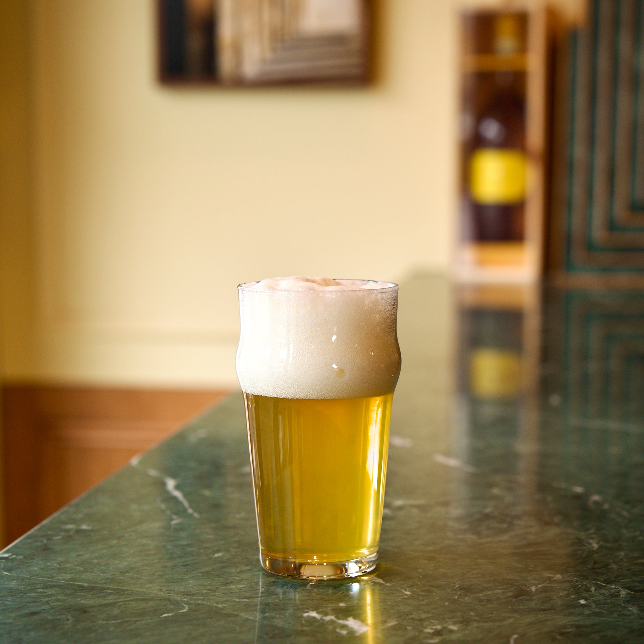 Nonix Beer glass with beer and foam on a green marble bar counter