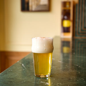 Nonix Beer glass with beer and foam on a green marble bar counter