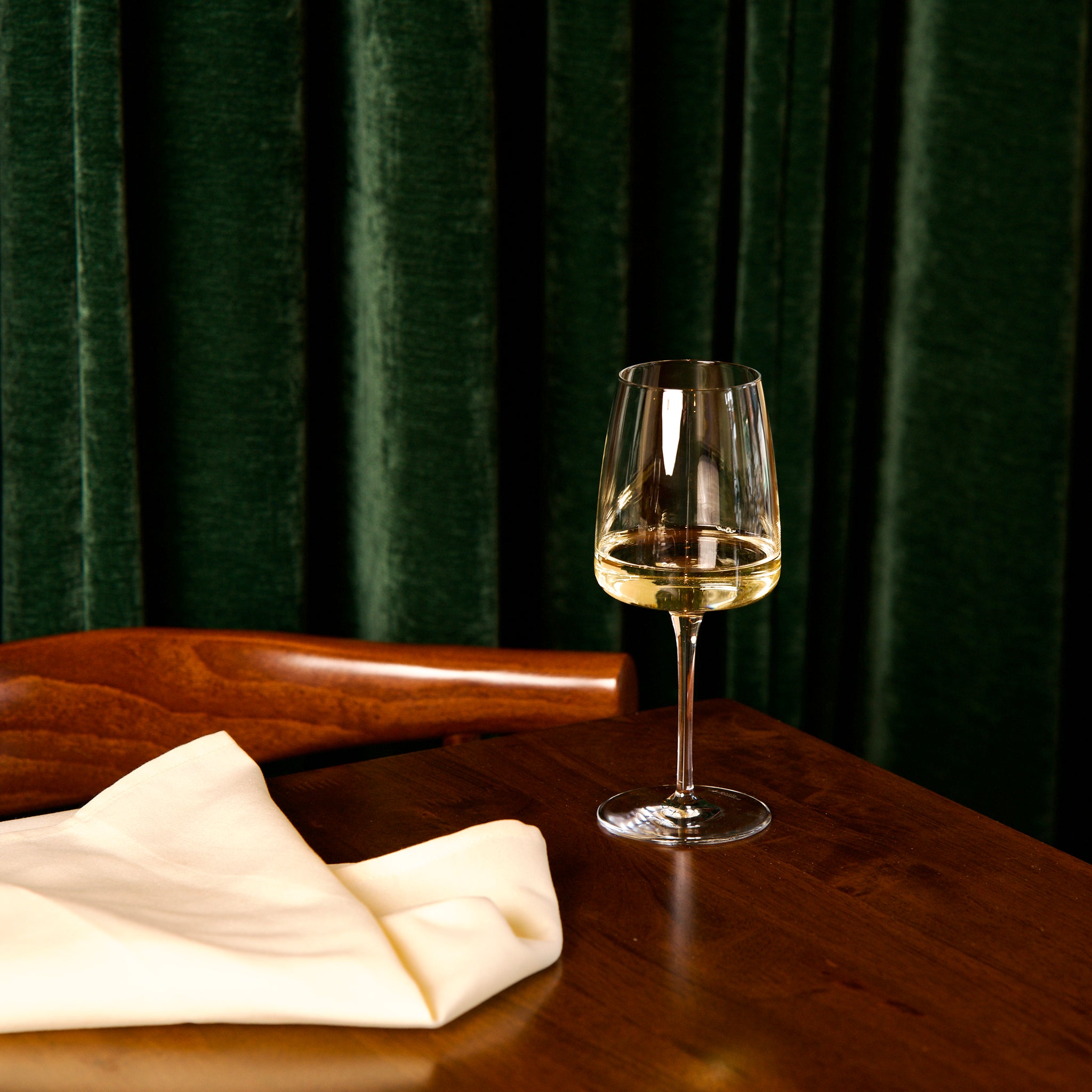 Planeo White Wine glass with white wine on a wooden table against a dark green curtain.