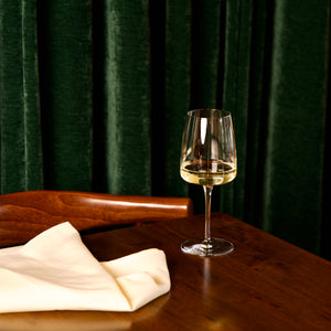 Planeo White Wine glass with white wine on a wooden table against a dark green curtain.