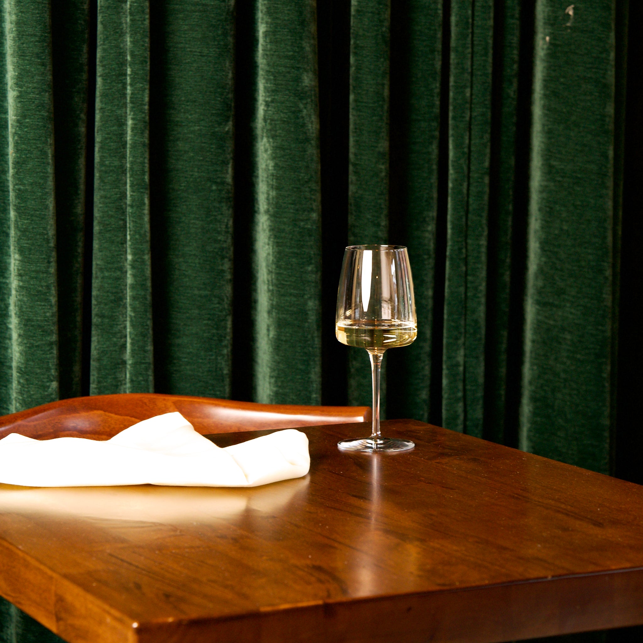 Planeo White wine glass filled with white wine standing on a wooden table with green curtain background
