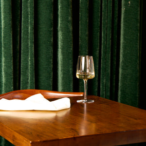 Planeo White wine glass filled with white wine standing on a wooden table with green curtain background