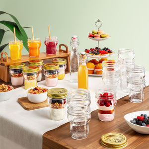 Table with Quattro Stagioni special edition jars of assorted drinks and snacks against a light green wall.
