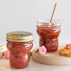 Two Quattro Stagioni special edition jars of red jam on a wooden board with a pink flower and toast.